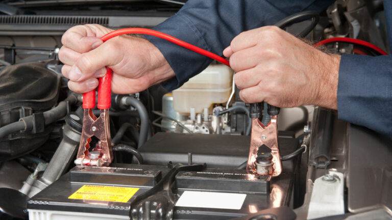 A car mechanic uses battery jumper cables to charge a dead battery.
